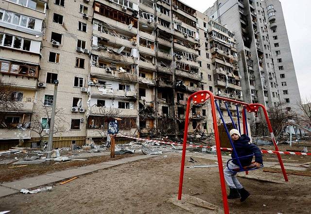 Criança brinca no que sobrou do parquinho de condomínio em Kiev
